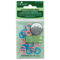 Clover brand Stitch Marker Rings in a clear plastic hanging package with a green header card. The rings are small in size, shown in pink, blue, and white, with a circular diagram on the packaging illustrating their use.