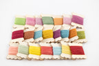 A set of 15 wooden spools of thread in various pastel and bright colors, arranged in a grid on a clean white background.