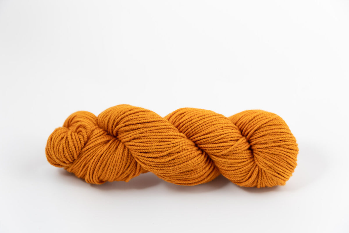 An orange skein of Shaniko wool and silk worsted weight yarn naturally dyed with marigold and sappanwood.