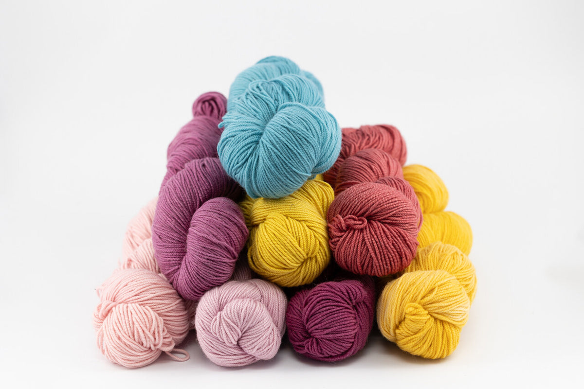 A stack of colorful yarn skeins in shades of blue, purple, pink, red, and yellow on a clean white background.
