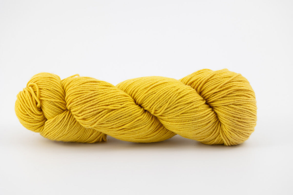 A yellow skein of Shaniko wool and silk yarn naturally dyed with orange osage. 