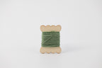 A green spool of merino tussah silk embroidery thread naturally dyed with chlorophyllin. 