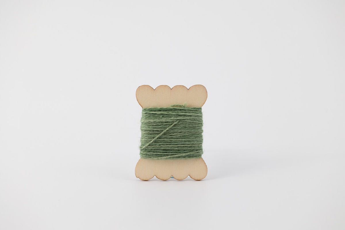 A green spool of merino tussah silk embroidery thread naturally dyed with chlorophyllin. 
