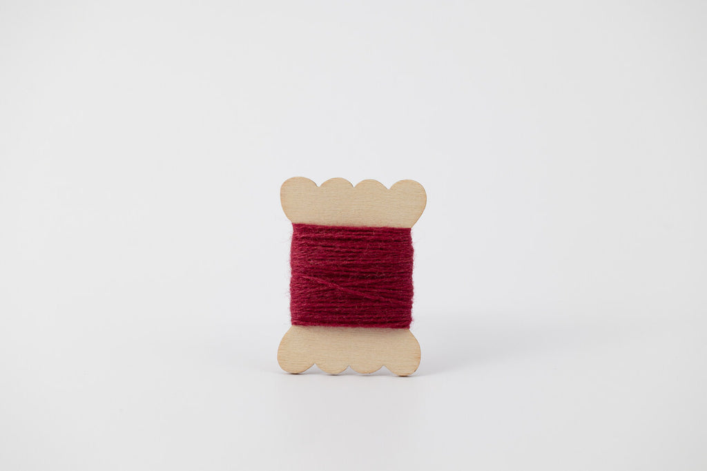 A dark pink spool of merino tussah silk embroidery thread naturally dyed with cochineal.