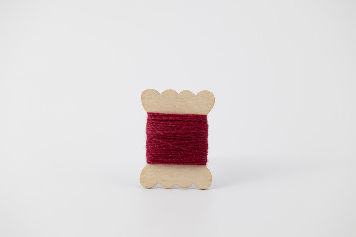 A dark pink spool of merino tussah silk embroidery thread naturally dyed with cochineal.