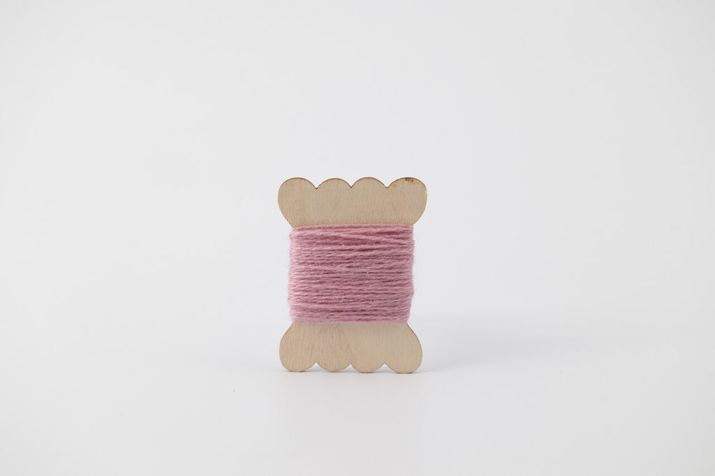A lavender spool of merino tussah silk embroidery thread naturally dyed with cochineal.