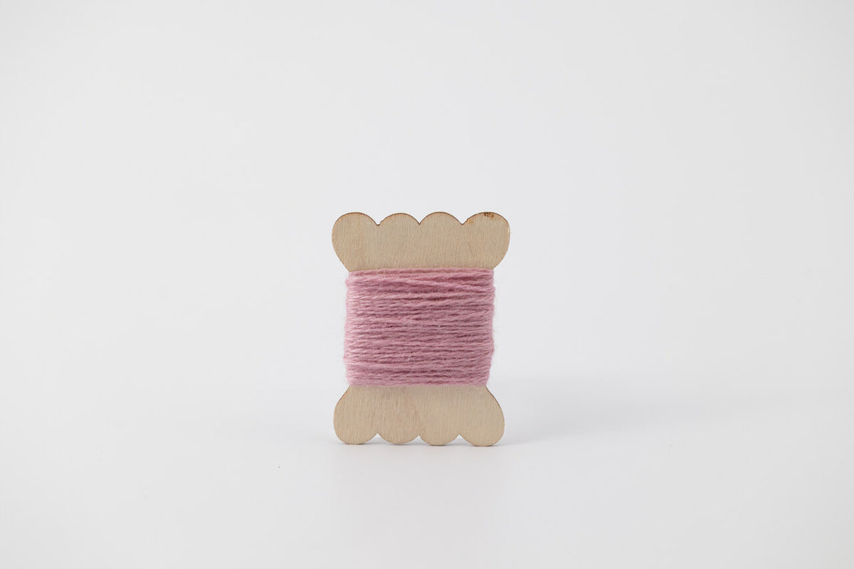 A lavender spool of merino tussah silk embroidery thread naturally dyed with cochineal.