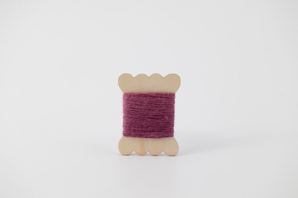 A purple spool of merino tussah silk embroidery thread naturally dyed with cochineal.