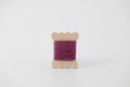 A purple spool of merino tussah silk embroidery thread naturally dyed with cochineal.