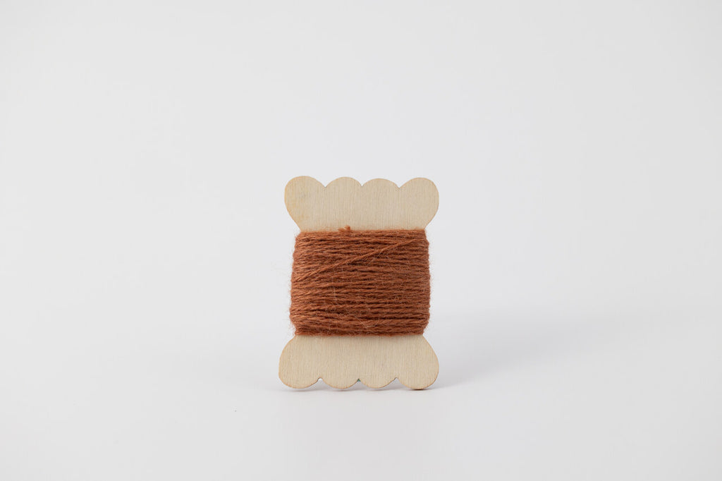 A brown spool of merino tussah silk embroidery thread naturally dyed with cutch.