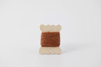 A brown spool of merino tussah silk embroidery thread naturally dyed with cutch.