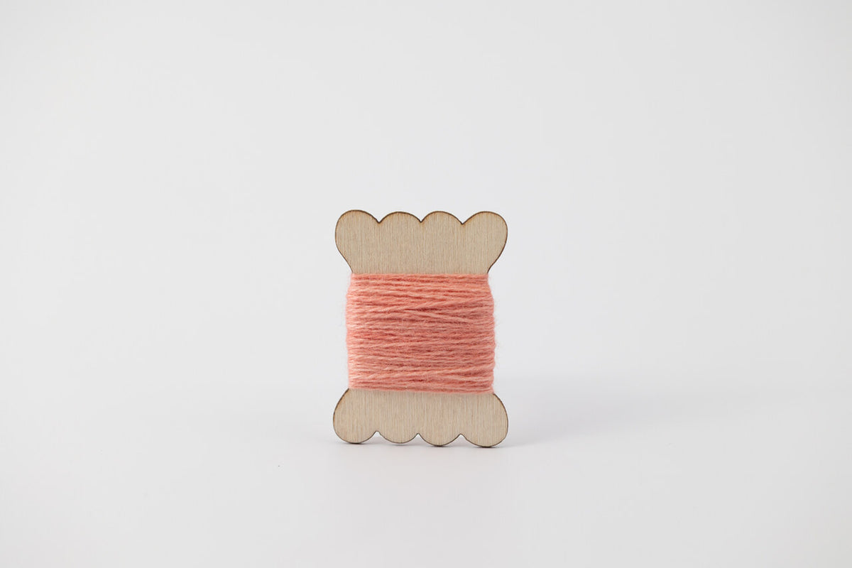 A light coral spool of merino tussah silk embroidery thread naturally dyed with madder root.