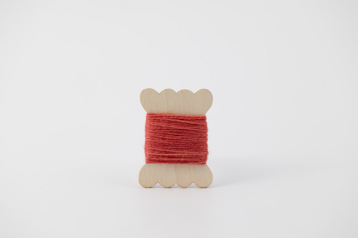 A dark coral spool of merino tussah silk embroidery thread naturally dyed with madder root.
