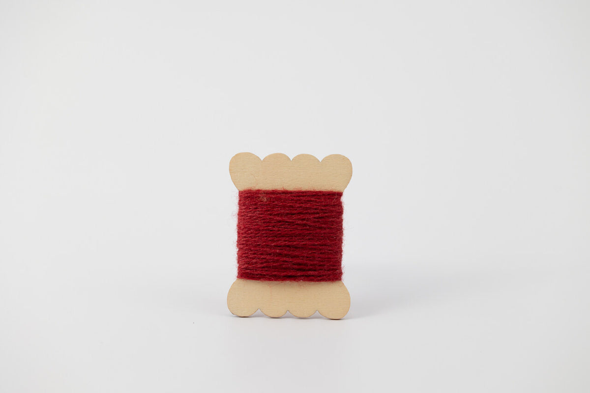 A red spool of merino tussah silk embroidery thread naturally dyed with madder root.