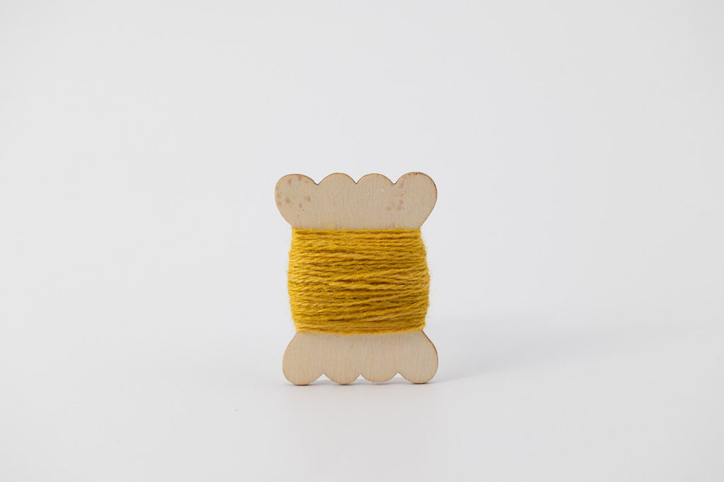 A yellow spool of merino tussah silk embroidery thread naturally dyed with marigold.