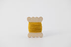 A yellow spool of merino tussah silk embroidery thread naturally dyed with marigold.