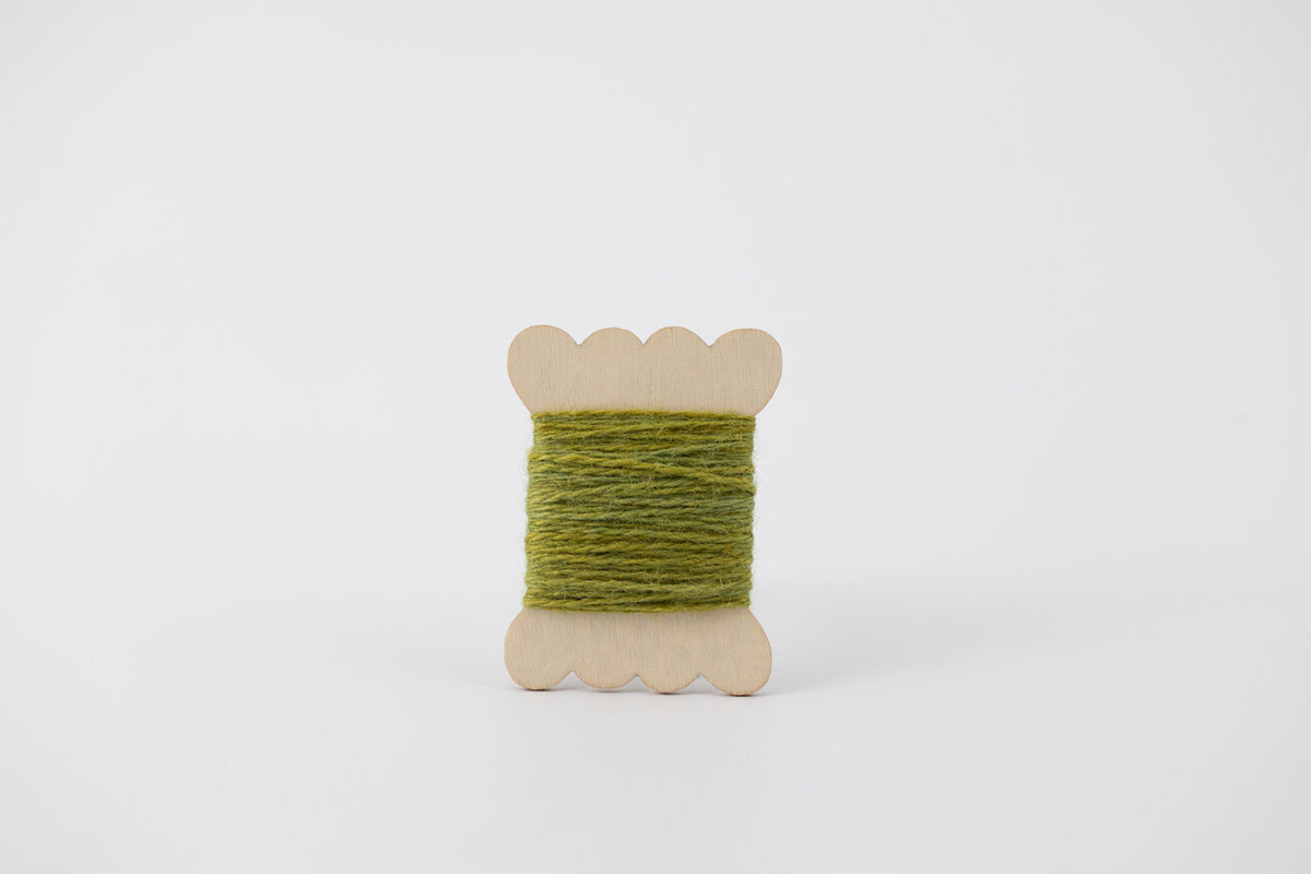 A green spool of merino tussah silk embroidery thread naturally dyed with indigo marigold.
