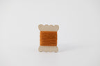 An orange spool of merino tussah silk embroidery thread naturally dyed with madder root and marigold.
