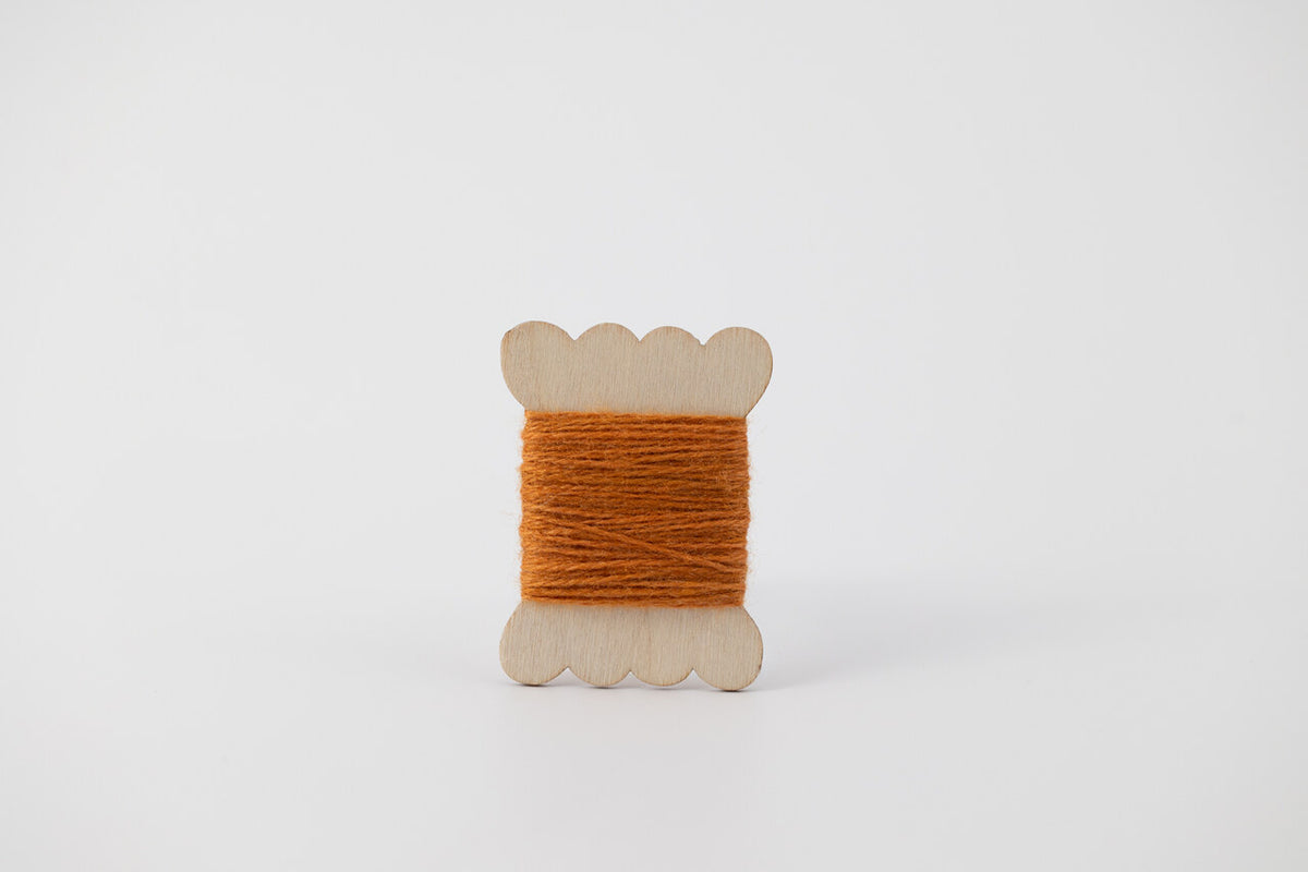 An orange spool of merino tussah silk embroidery thread naturally dyed with madder root and marigold.