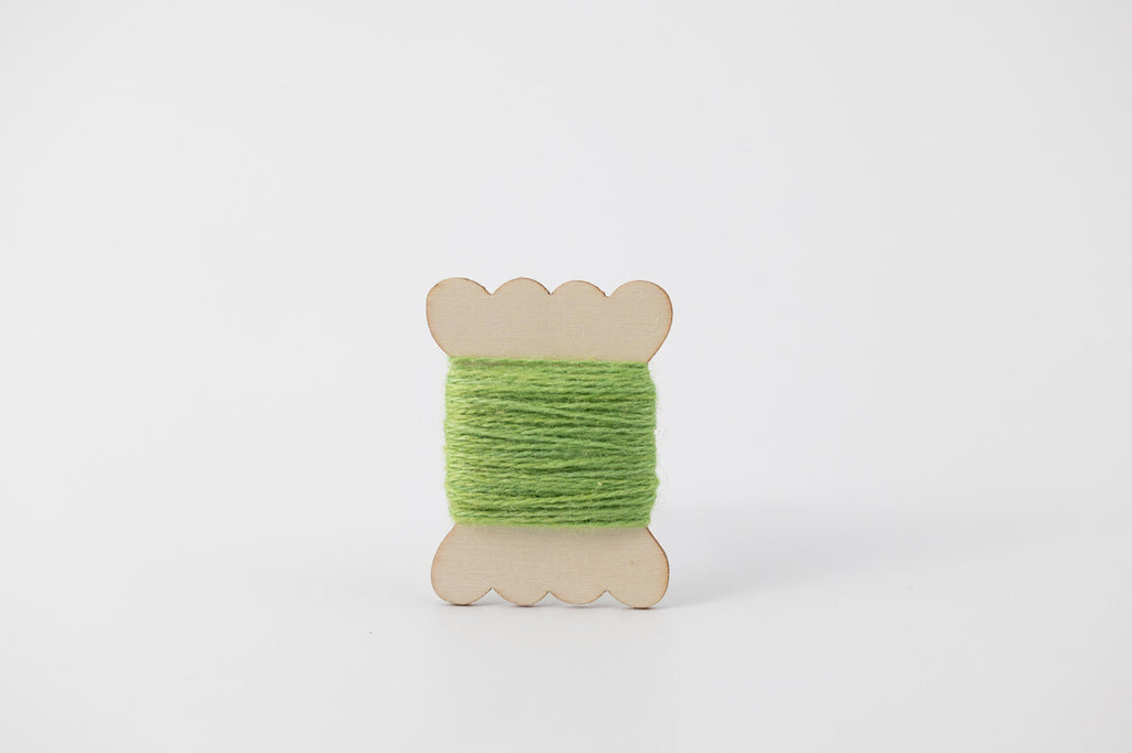 A bright green spool of merino tussah silk embroidery thread naturally dyed with weld and indigo. 