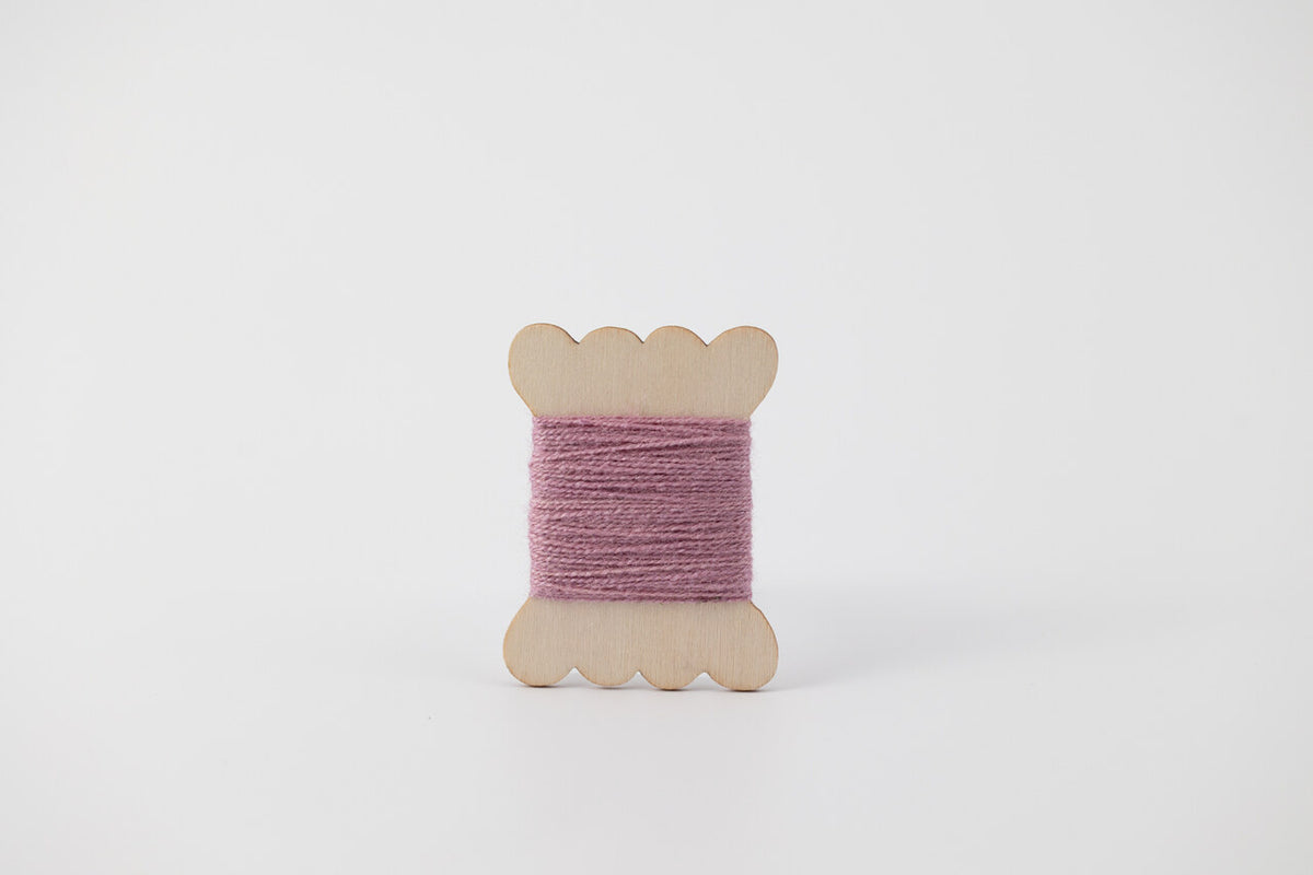 A bobbin of tussah silk embroidery dyed with cochineal to a lavender color.