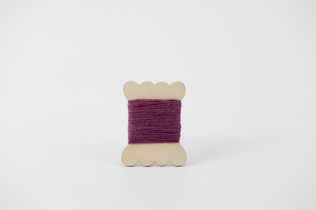 A bobbin of tussah silk embroidery dyed with cochineal to a purple color.