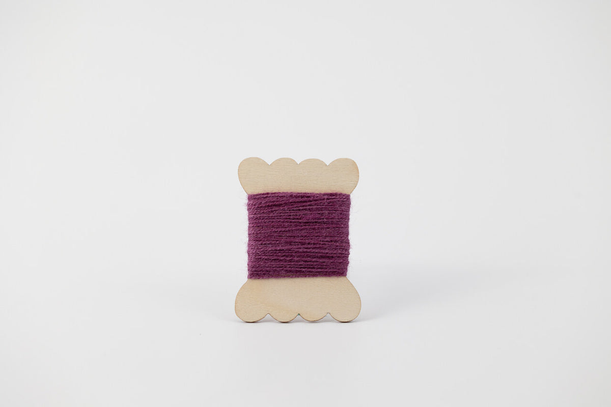 A bobbin of tussah silk embroidery dyed with cochineal to a purple color.