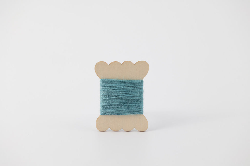 A bobbin of tussah silk embroidery dyed with indigo to a light blue color.