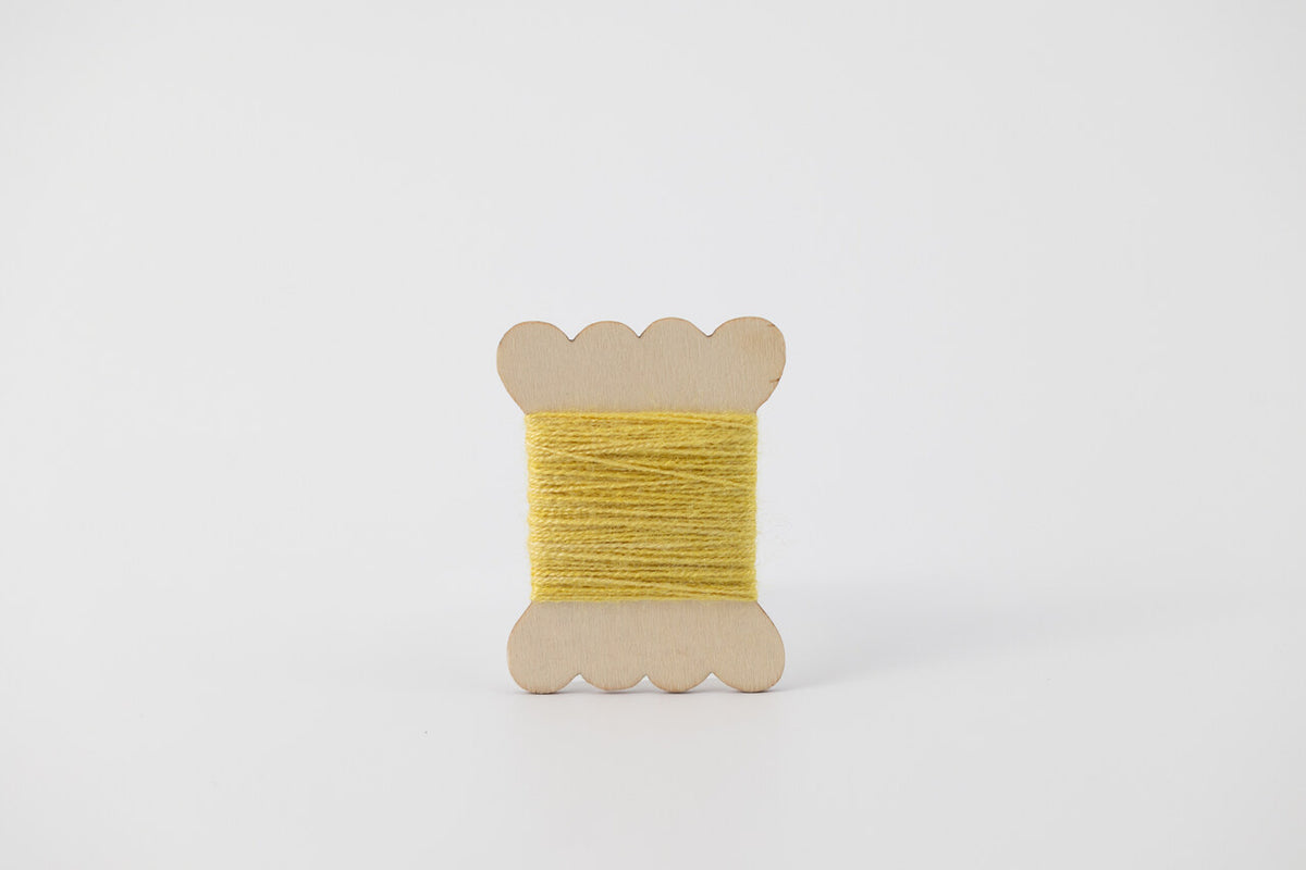 A bobbin of tussah silk embroidery dyed with weld to a yellow color.