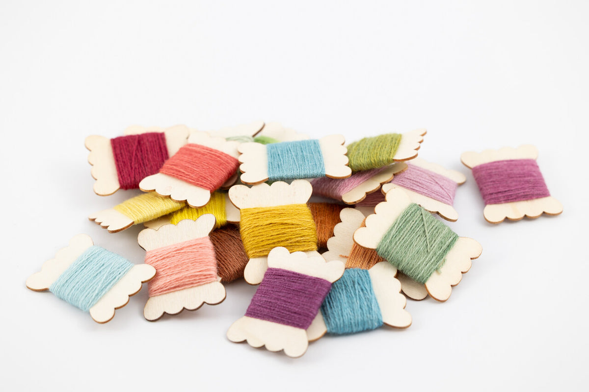 A pile of small wooden spools of thread in assorted colors, including purple, blue, pink, yellow, green, and brown, arranged on a plain white background.