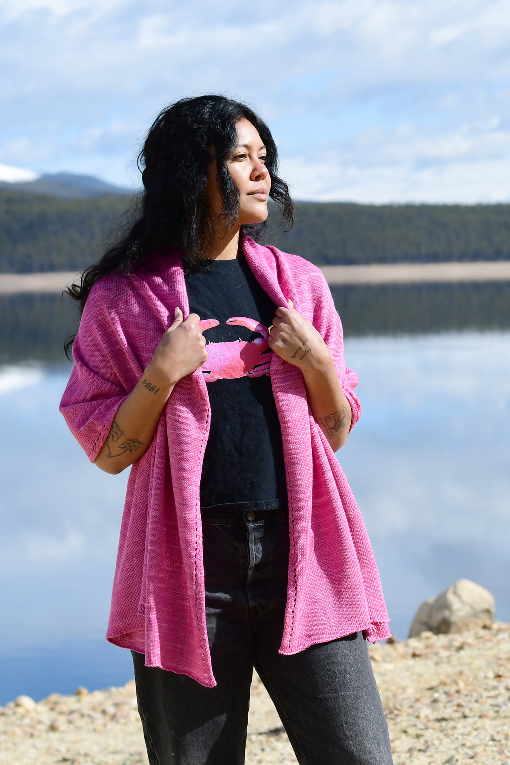 A woman wearing a pink scarf that is made of merino and silk and naturally dyed with cochineal.