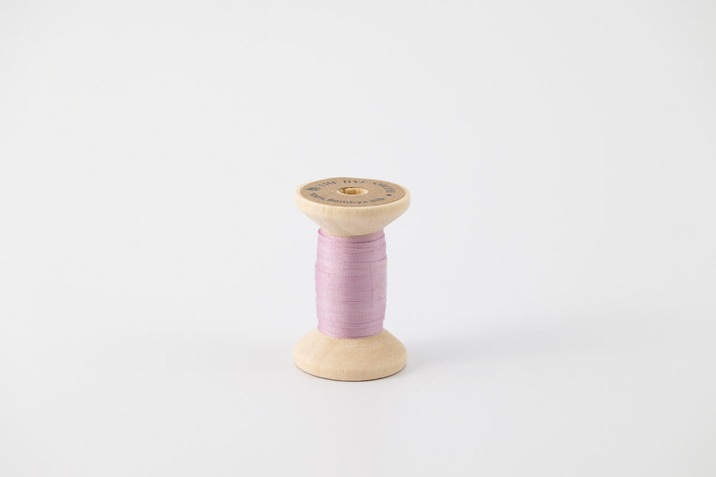 A spool of naturally dyed silk ribbon dyed with cochineal to a lavender color.