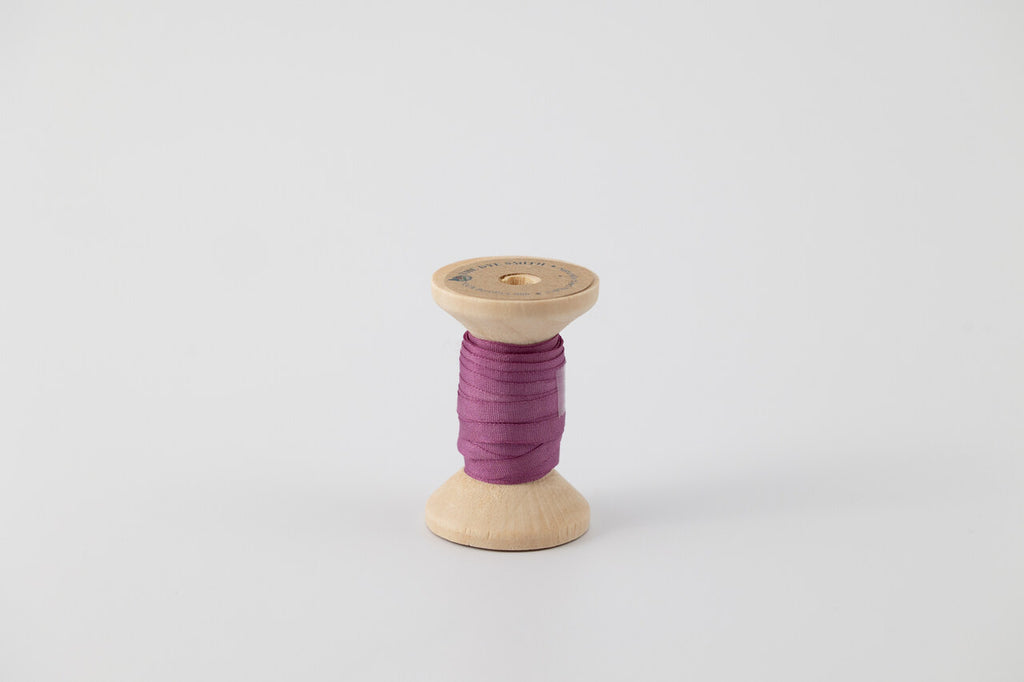 A spool of naturally dyed silk ribbon dyed with cochineal to a purple color.
