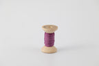A spool of naturally dyed silk ribbon dyed with cochineal to a purple color.