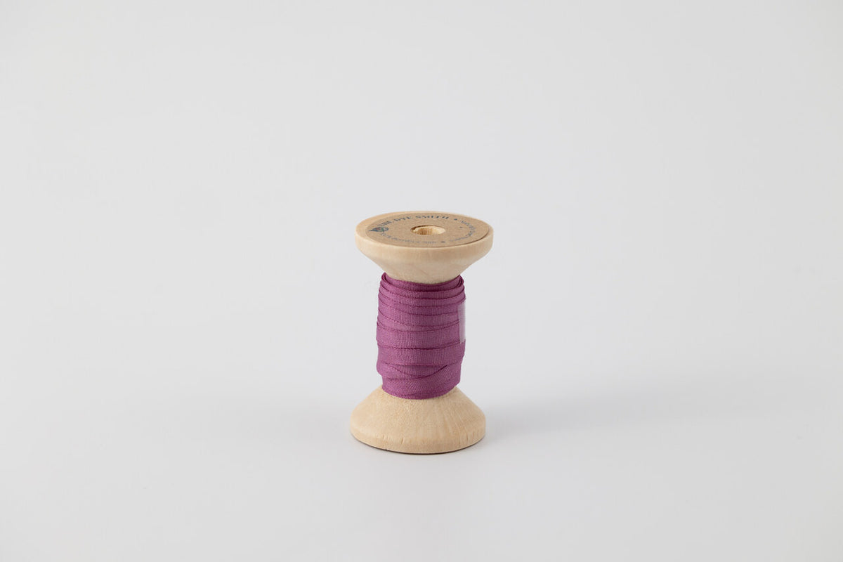 A spool of naturally dyed silk ribbon dyed with cochineal to a purple color.