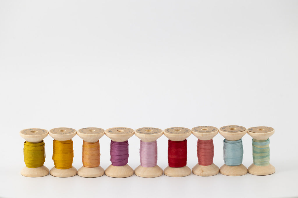 Nine spools of naturally dyed silk ribbon in different colors.