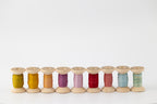 Nine spools of naturally dyed silk ribbon in different colors.