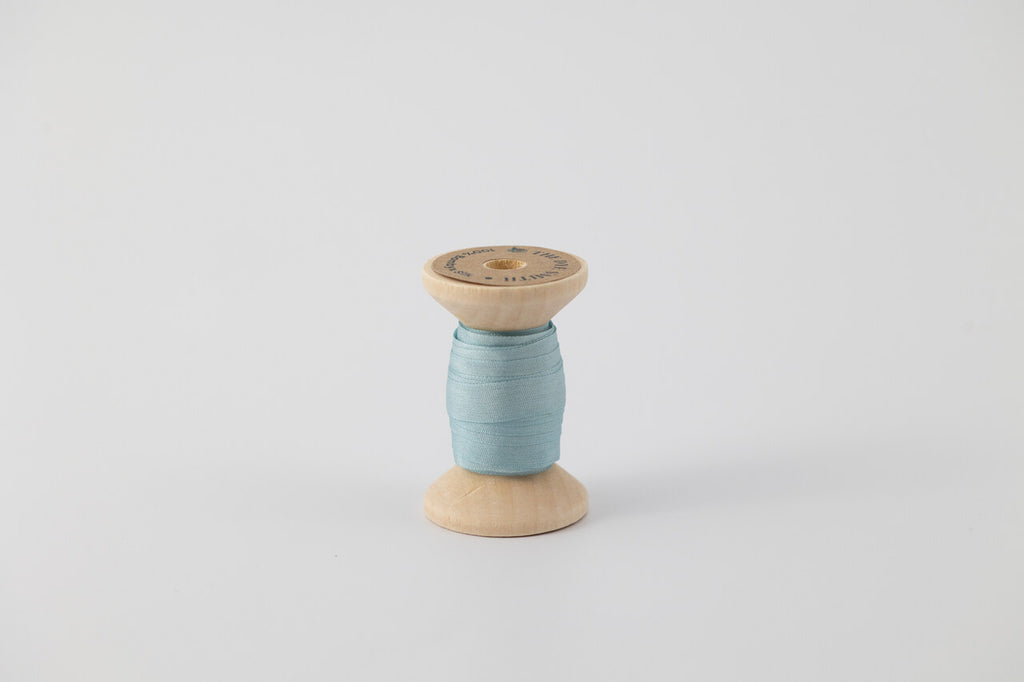 A spool of naturally dyed silk ribbon dyed with indigo to a light blue color.