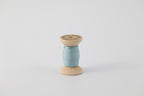 A spool of naturally dyed silk ribbon dyed with indigo to a light blue color.