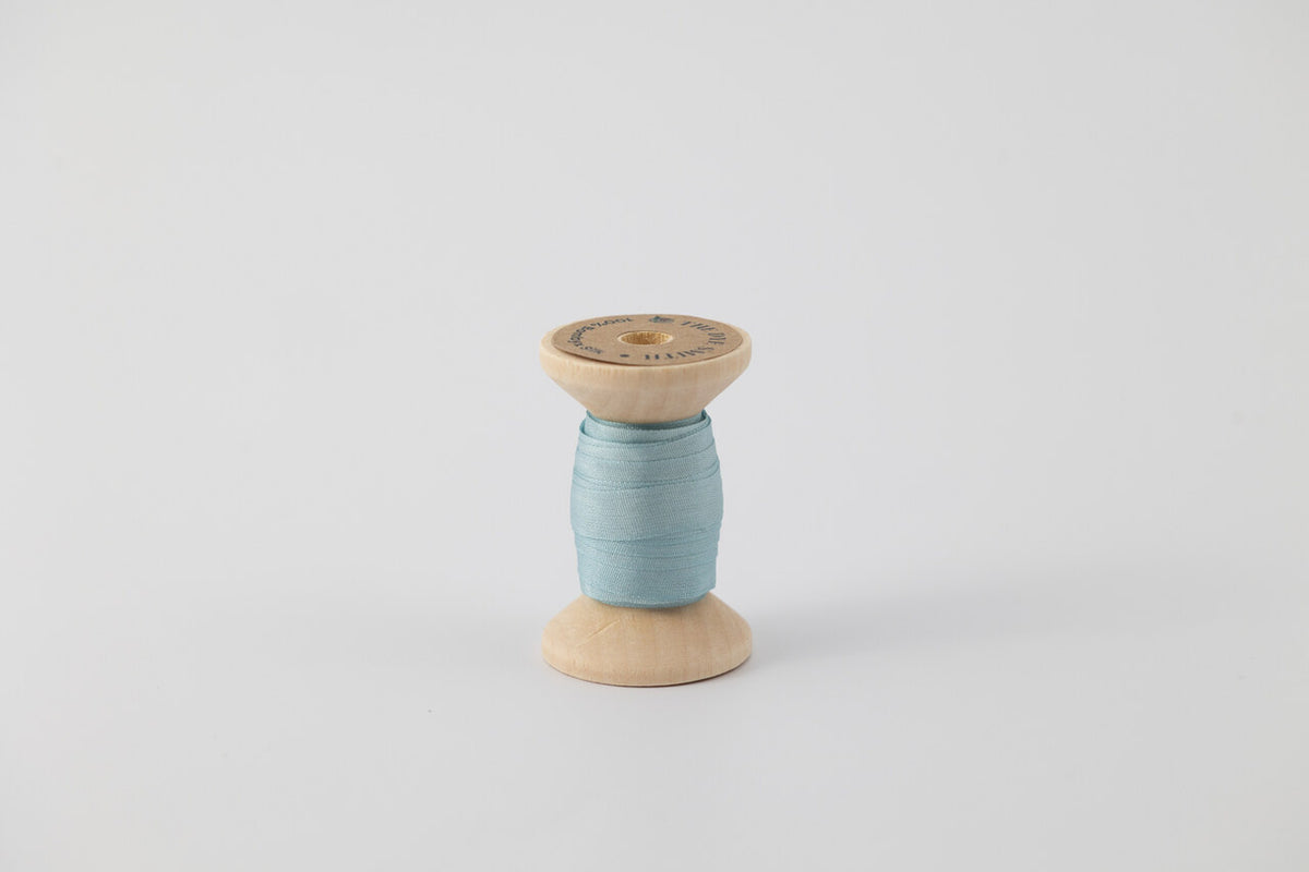 A spool of naturally dyed silk ribbon dyed with indigo to a light blue color.
