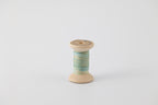A spool of naturally dyed silk ribbon dyed with indigo and pomegranate. Multi colored with blue, green, and yellow. 