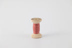 A spool of naturally dyed silk ribbon dyed with madder to a dark coral color.