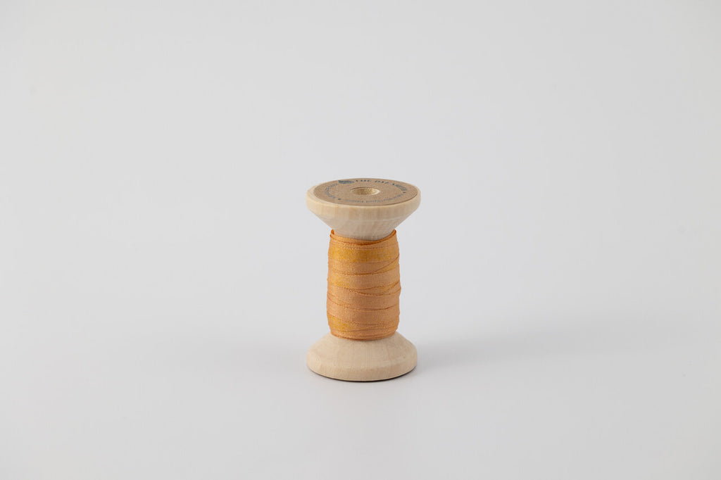 A spool of naturally dyed silk ribbon dyed with madder root and marigold to an orange color.