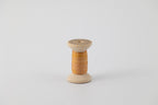 A spool of naturally dyed silk ribbon dyed with madder root and marigold to an orange color.