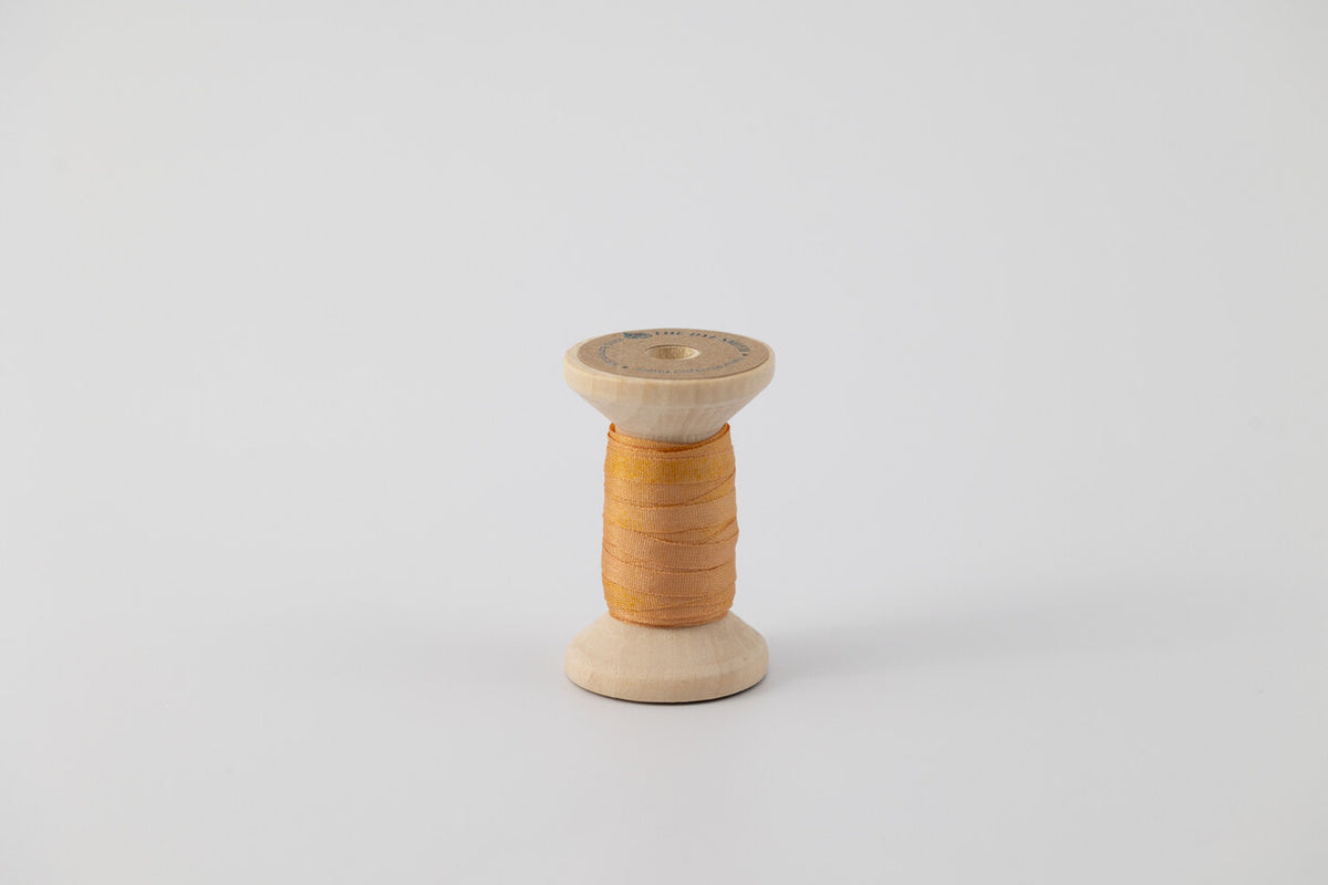 A spool of naturally dyed silk ribbon dyed with madder root and marigold to an orange color.