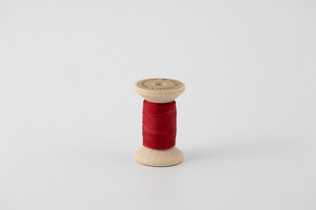 A spool of naturally dyed silk ribbon dyed with madder root to a deep red color.