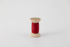 A spool of naturally dyed silk ribbon dyed with madder root to a deep red color.