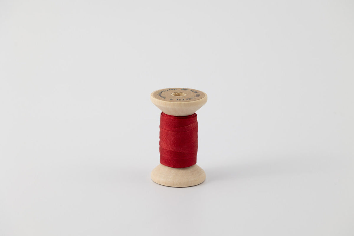 A spool of naturally dyed silk ribbon dyed with madder root to a deep red color.