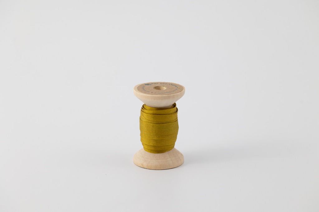 A spool of naturally dyed silk ribbon dyed with indigo and marigold to a chartreuse color.  