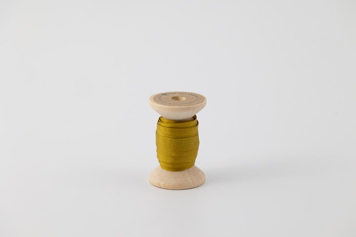 A spool of naturally dyed silk ribbon dyed with indigo and marigold to a chartreuse color.  